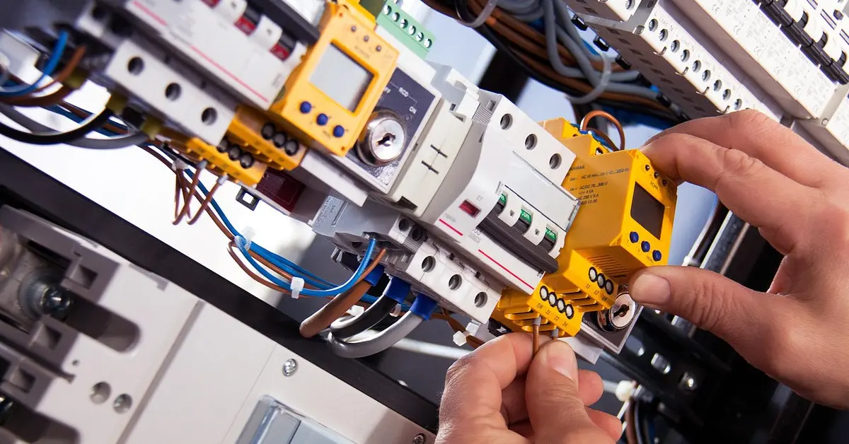 Elektryk pracujący przy domowej rozdzielnicy elektrycznej, podłączający przewody do modułów zabezpieczeń i sterowników.